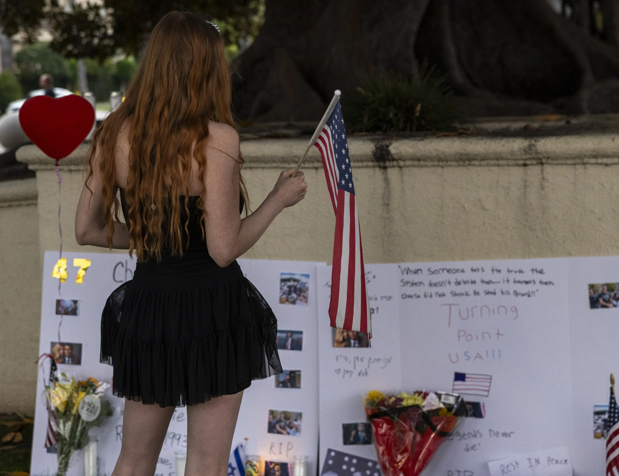 A woman holds an American flag and stares at a vigil sign dedicated to Charlie Kirk during a vigil, on Sunday, Sept 14, 2025, in Beverly Hills, Calif., following Charlie Kirk’s assassination. (Jake Crandall | The Corsair)