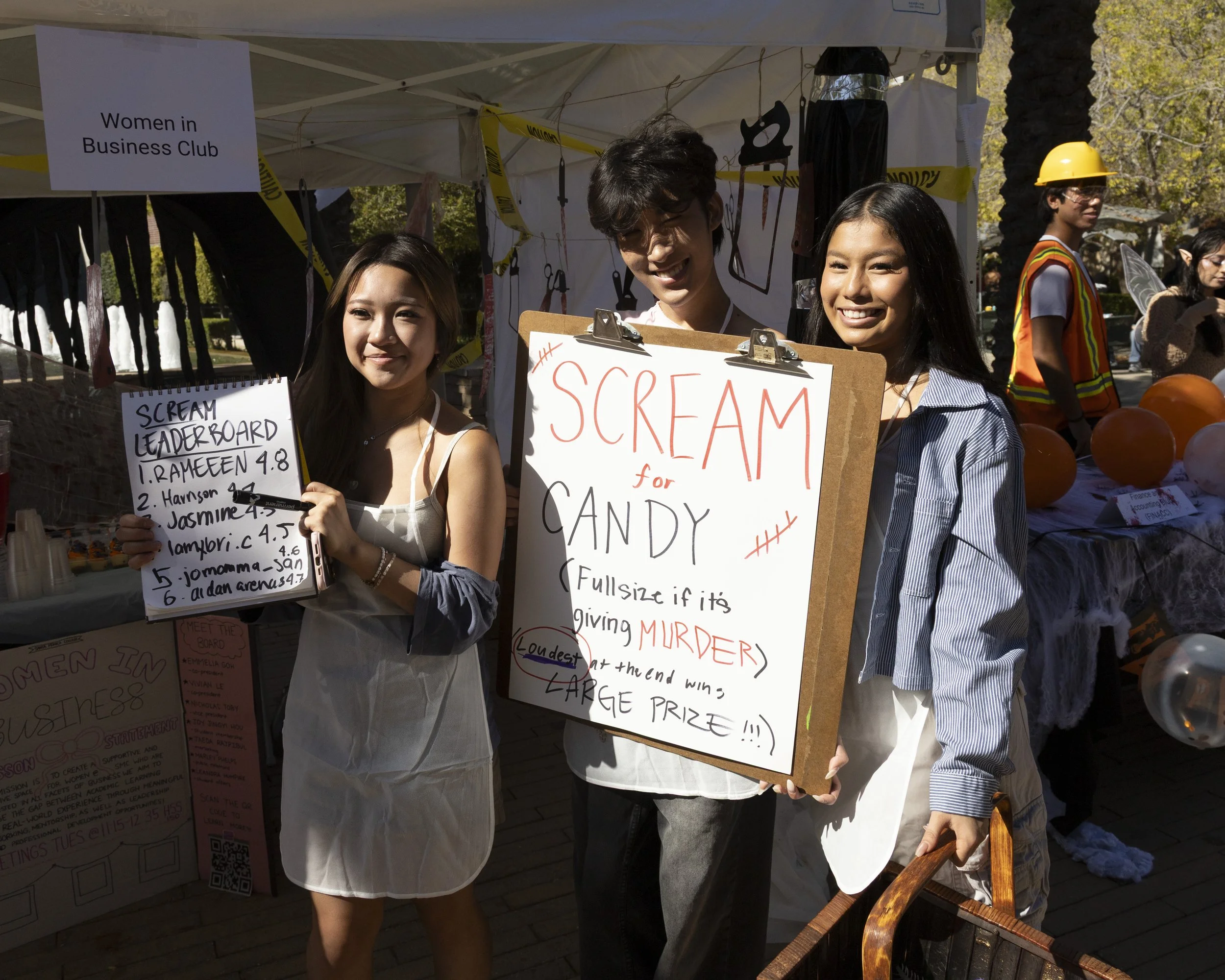  Vivian Le (left), Nicky Wang (center), and Jaeda Rajpilour (right) (all cq) of the Women in Business Club pose with their sign and leaderboard at Club Row on the campus of SMC in Santa Monica, Calif., Thursday, October 30, 2025. The Women in Busines