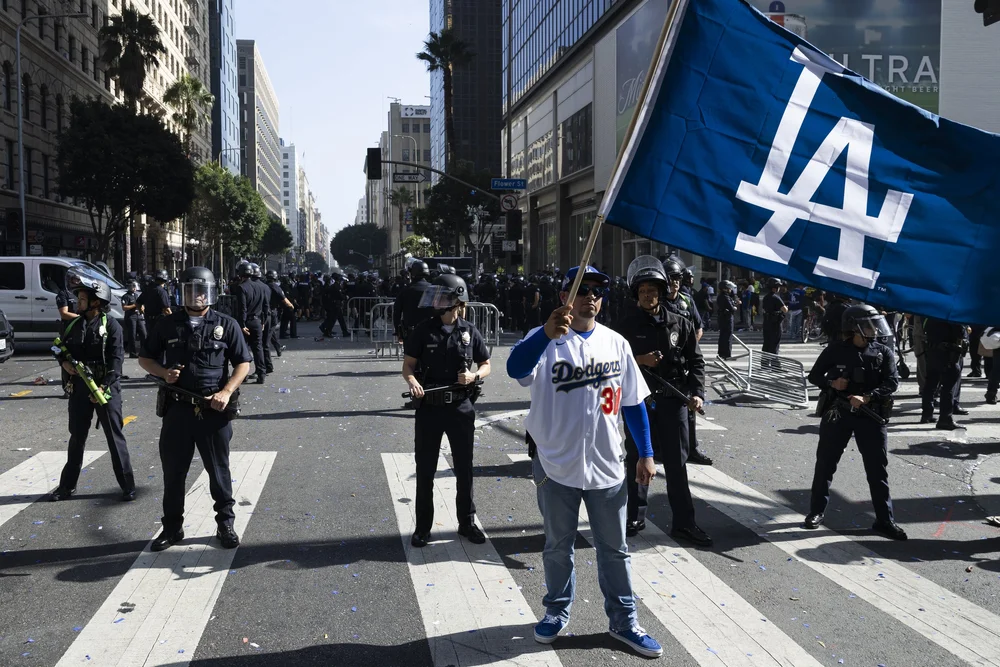  A Los Angeles Dodgers fan holds up a Dodgers flag in front of the Los Angeles Police Department after they declared an unlawful assembly following the Dodgers’ World Series Championship Parade on Monday, Nov. 3, 2025, in downtown Los Angeles. (Jake 