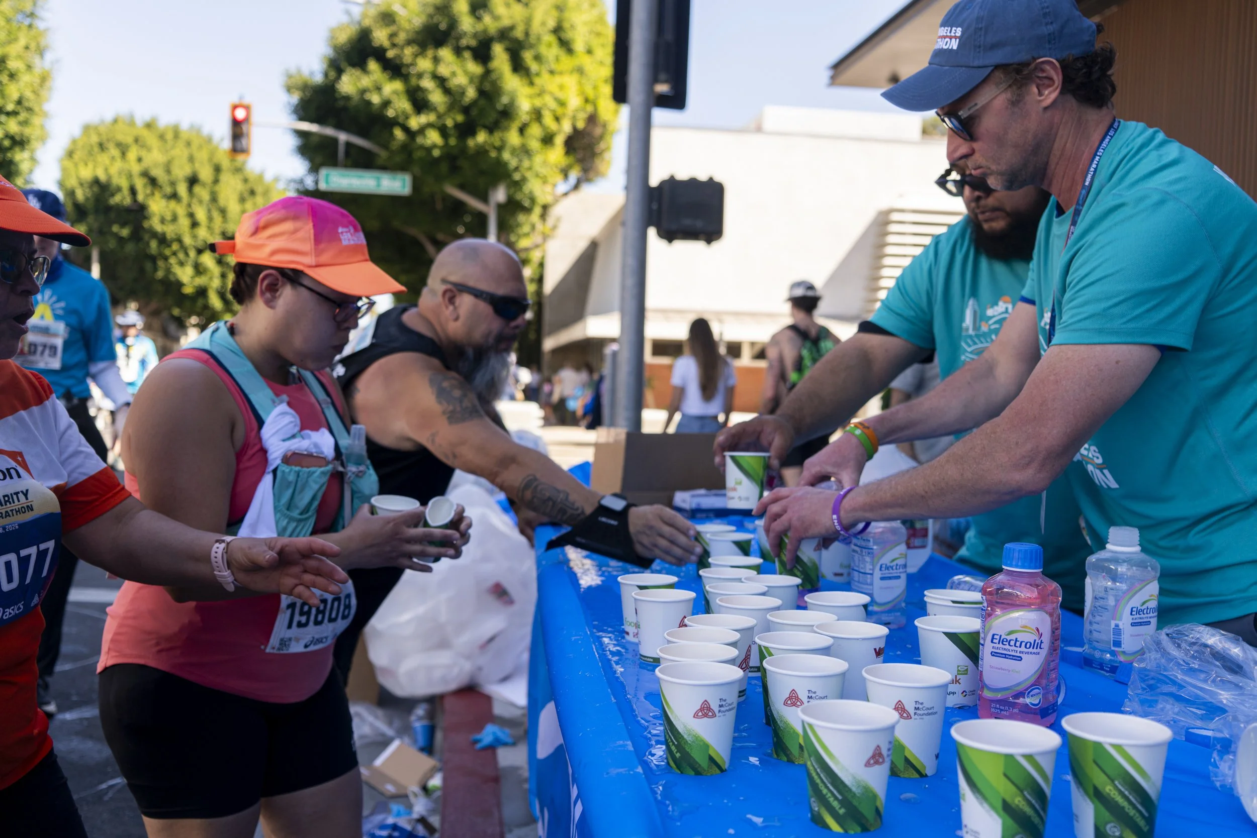  First year vloenteer Ben Christain (far right) & ten year Los Angeles Marathon runner veteran races to fill cups as runners gather for refreshments at mile 17 water station at the cross streets of Charleville Blvd and Santa Monica Blvd at the 41st a