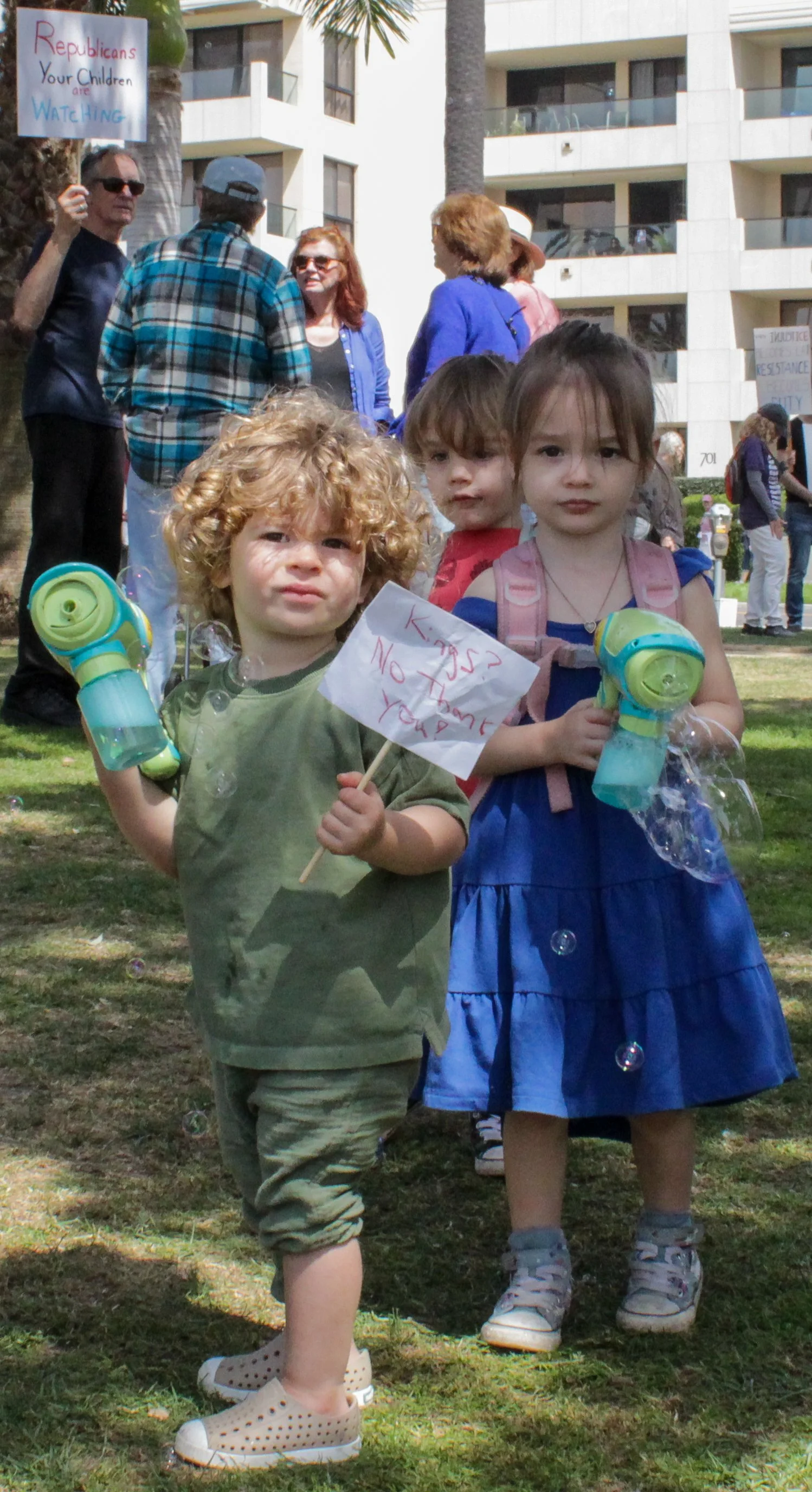  Oelsen Rosenberg, 2, left, and twins Logan, center, and Aurora Sullivan, right, 2, play with bubble machine guns and hold a mini protest sign at the No Kings protest at Palisades Park in Santa Monica, Calif., on March 28, 2026. (Caelen Perkins | The