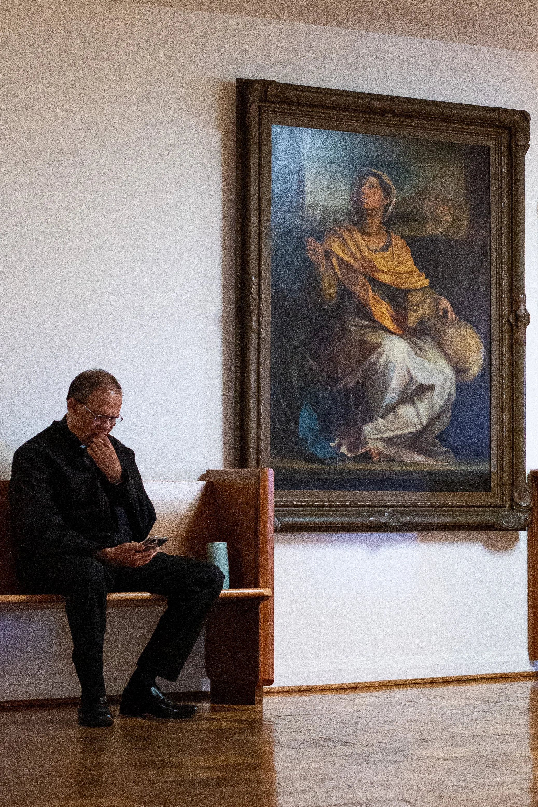  Father Valerian Menezes, associate pastor of Corpus Christi Church, sits in the lobby of St. Joseph’s Chapel at the Carondelet Center near a painting of St. Agnes—a 4th-century martyr and symbol of purity—following Easter Sunday Mass, Sunday, April 