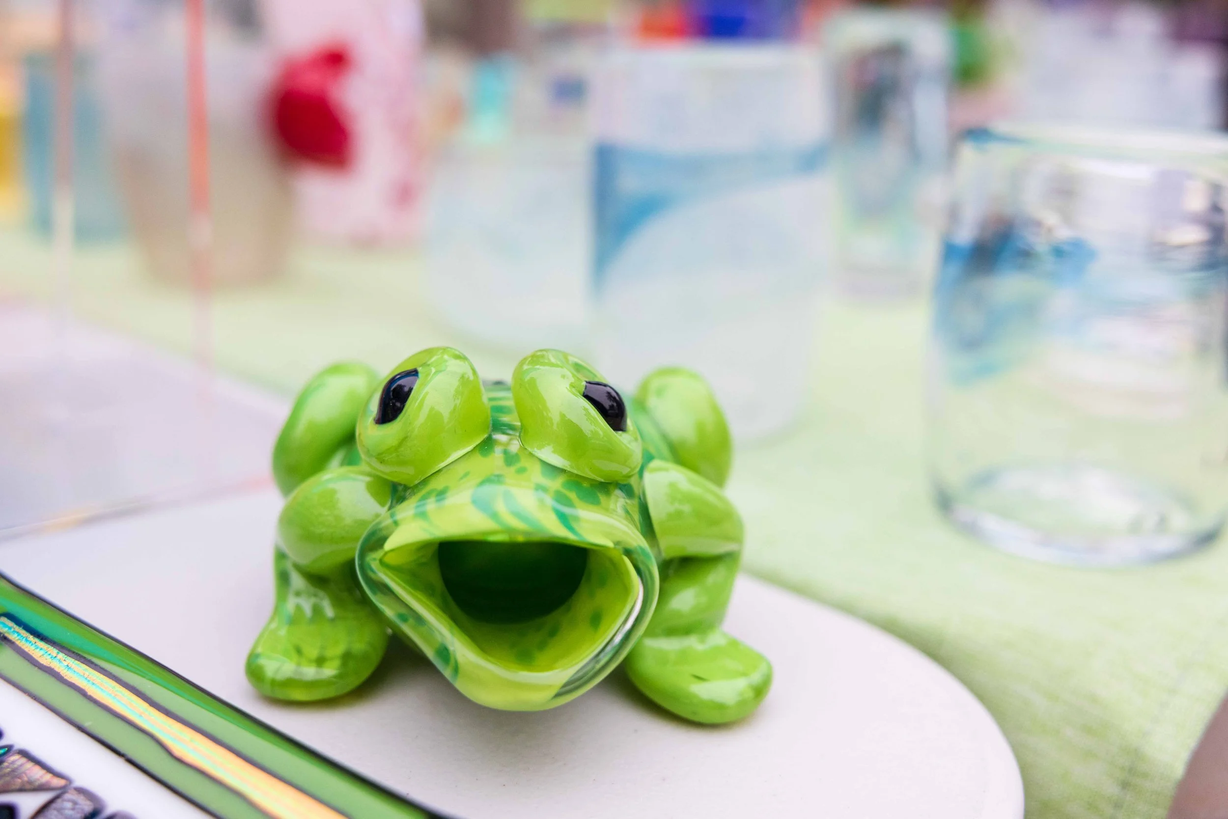  A green glass frog by Santa Monica College (SMC) instructor Terri Bromberg in front of several glass pieces by glass blowing student Haneul Park during the SMC Art Department's Mother's Day Glass Sale at Virginia Park Farmers Market in Santa Monica,