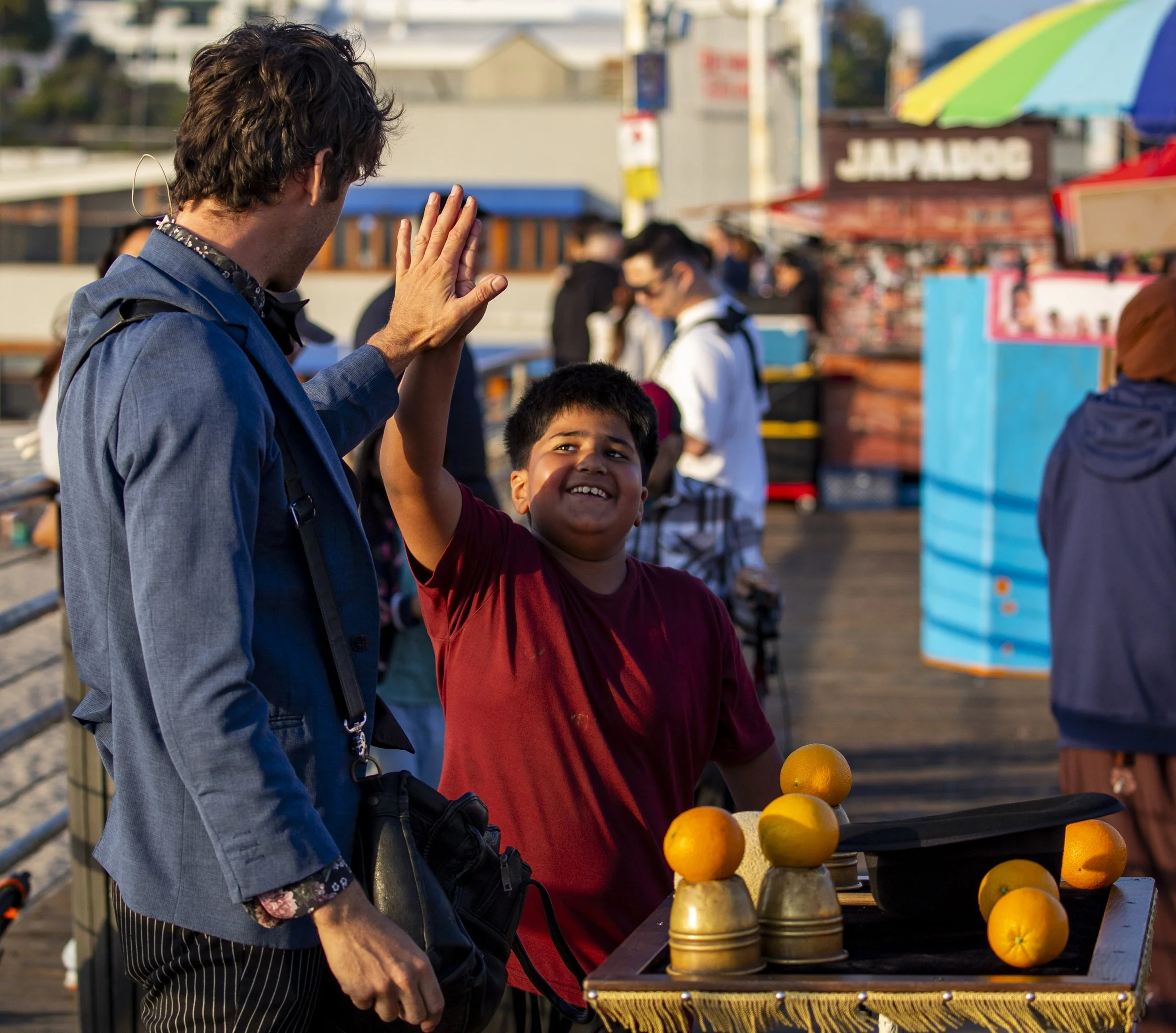  Street magician Jesse Mock high-fives a child who helped him perform a cups-and-balls trick at the Santa Monica Pier in Santa Monica, Calif., on Friday, May 1, 2026. Mock used three metal cups to make several oranges appear throughout the trick befo