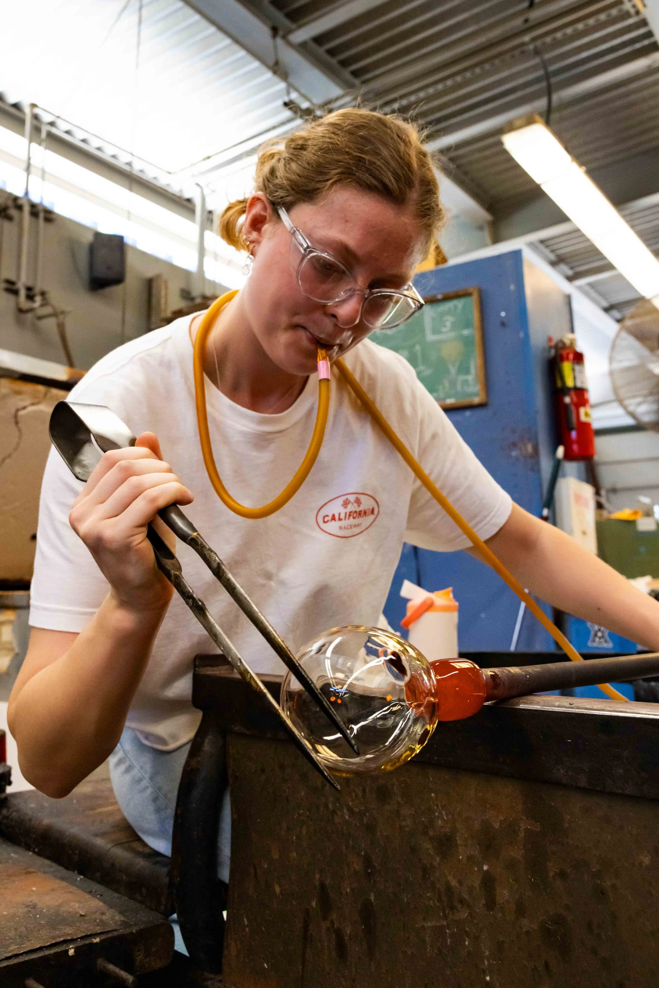  Santa Monica College (SMC) student Emily Trief uses a blow hose to blow glass while simultaneously shaping it with tweezers inside the hot shop at the SMC arts complex in Santa Monica, Calif., Friday, May 29, 2026. (Elizabeth Bacher | The Corsair) 