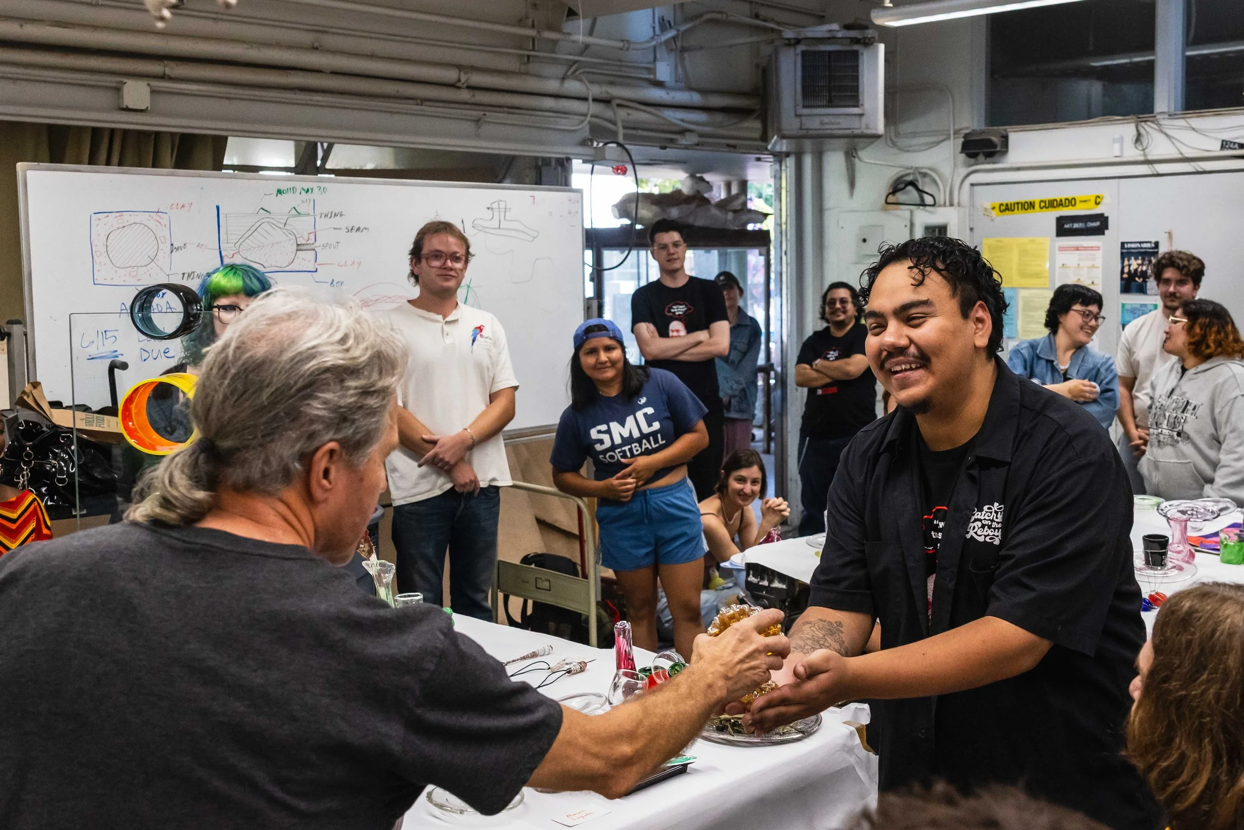  Santa Monica College (SMC) student Ernesto Navarro (center) receives the "Golden Waffle," an award bestowed on one student by the laboratory technicians, from technician Andy Berney (L) during final presentations by the spring glass scultupre class 