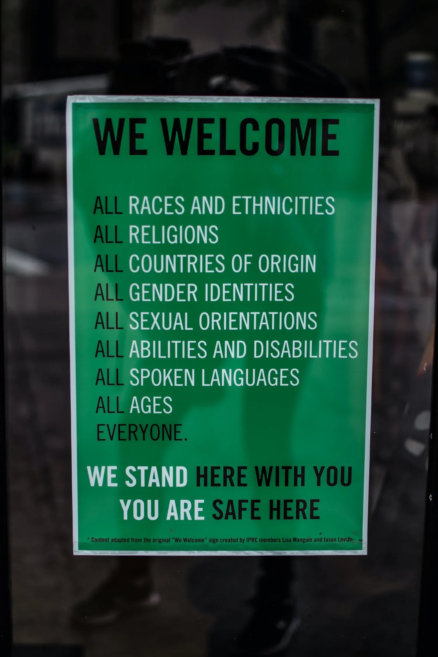 Green We Welcome sign in a window welcoming all races, religions, countries of origin, sexual orientations, genders, abilities, languages and ages