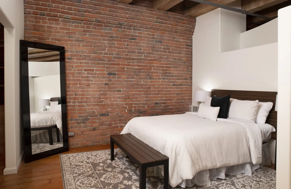 Primary bedroom with brick wall and white linens