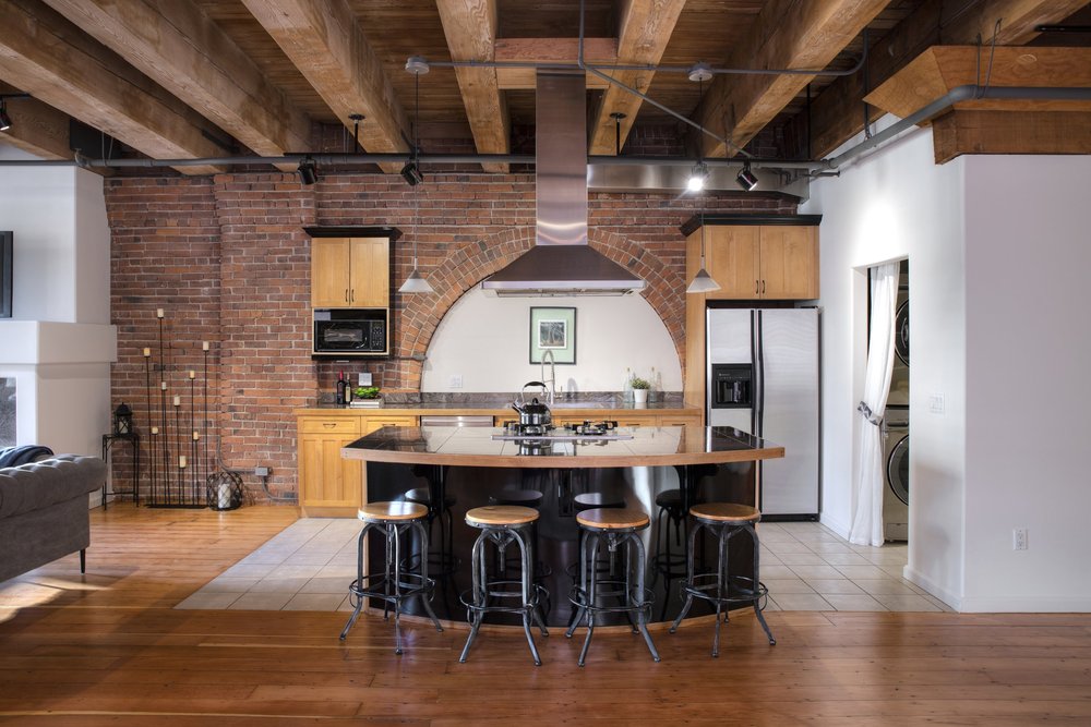 Loft kitchen with brick walls and timber beams, photographed for a Brian Huie listing