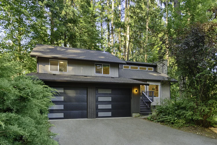 Moss + Modern exterior in Woodinville with black two-car garage doors and tall evergreens