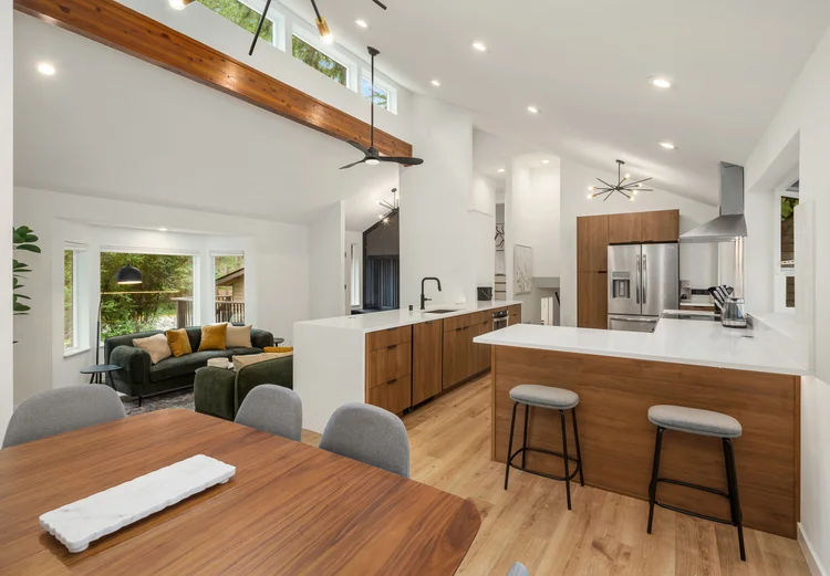 Open great room with dining table, walnut kitchen and green sofa under vaulted wood beam