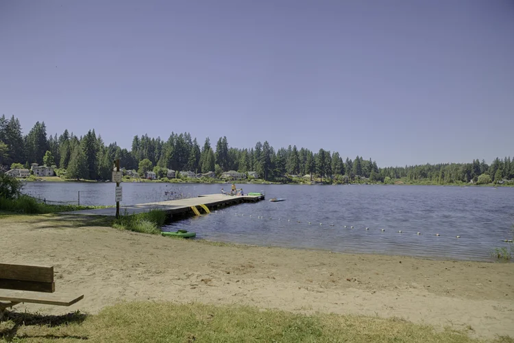 Sandy beach at Cottage Lake Beach Club with bench, swim dock and treeline beyond