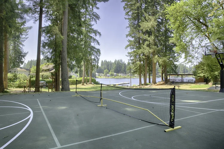 Sport court with pickleball net and basketball hoop near Cottage Lake under tall firs