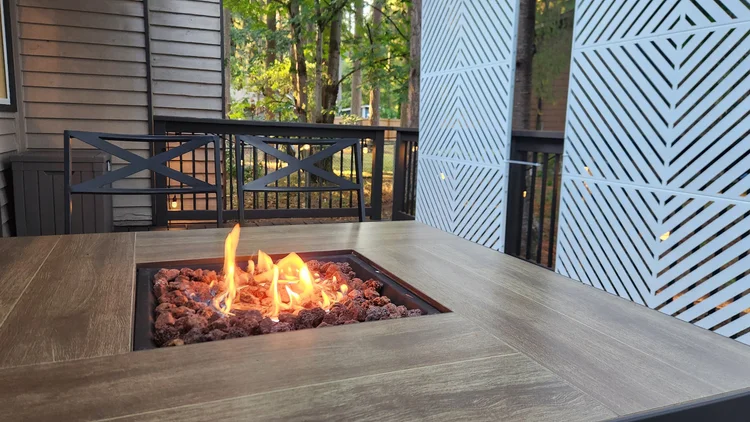 Gas fire table burning on a deck with geometric privacy screens and trees beyond
