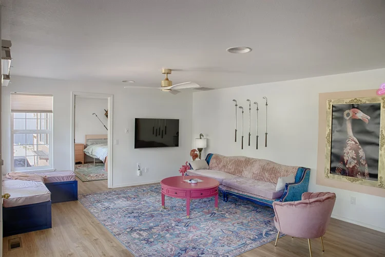 Living room with pink round coffee table, blue sofa and a view into a bedroom