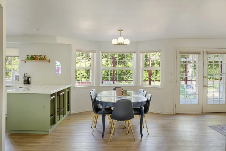 Dining nook with oval table, globe chandelier and three windows beside French doors