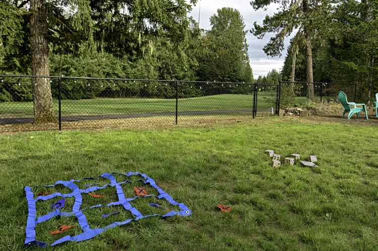 Backyard lawn games, a giant ring toss mat and wooden blocks, beside the golf course fence