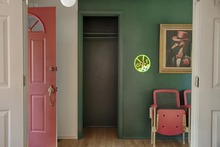 Entry with pink front door, green accent wall, flamingo portrait, golf neon sign and theater seats