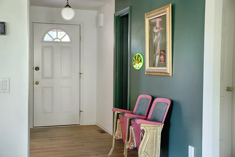 Front entry hall with pink vintage theater seats below a gold-framed flamingo painting on a green wall