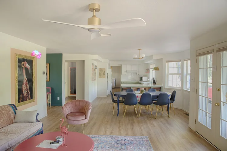 Open living room with pink coffee table, blush armchair, flamingo portrait and dining area beyond