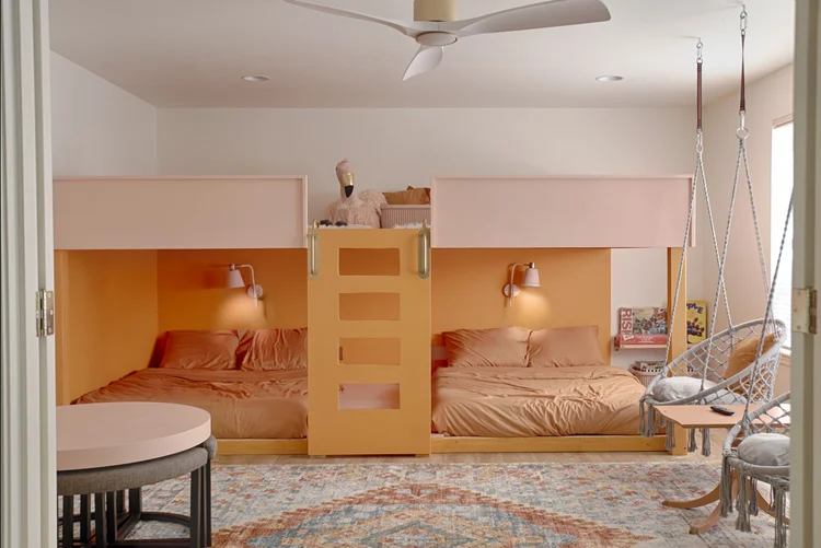Bunk room with two built-in peach beds, wall sconces and two hanging chairs
