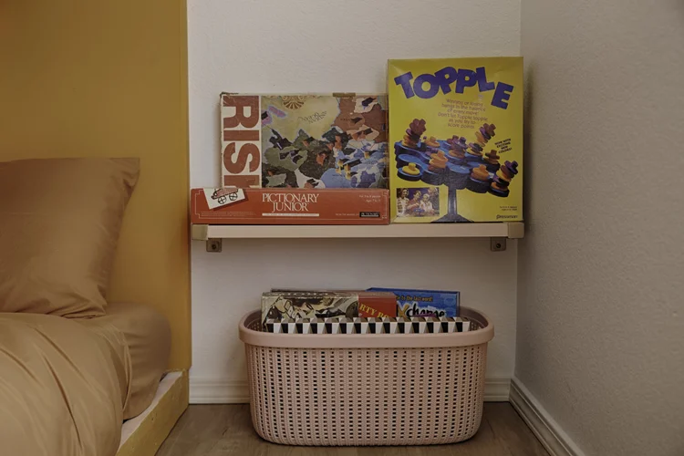 Board games on a shelf beside a bunk bed, with a basket of more games below