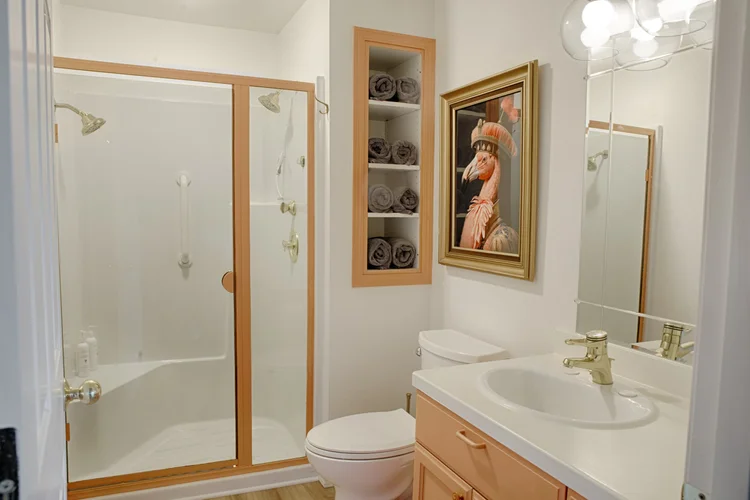 Bathroom with glass shower, rolled towels in a wall niche and a framed flamingo portrait