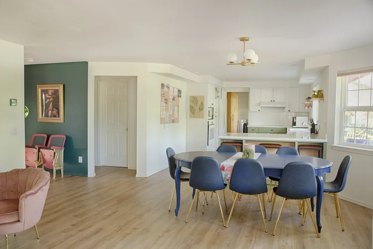 Open dining area with oval table and navy chairs leading to a green kitchen with breakfast bar