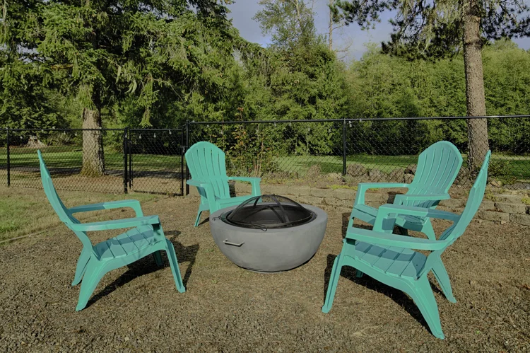 Four teal Adirondack chairs around a round fire pit in the fenced backyard