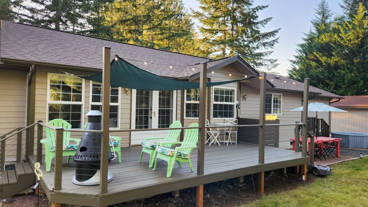 Back deck with shade sail, green Adirondack chairs and a chimney fire pit