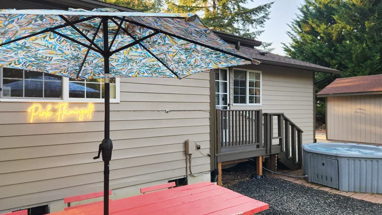 Back patio with red picnic table, patterned umbrella, Pink Flamingolf neon sign and hot tub