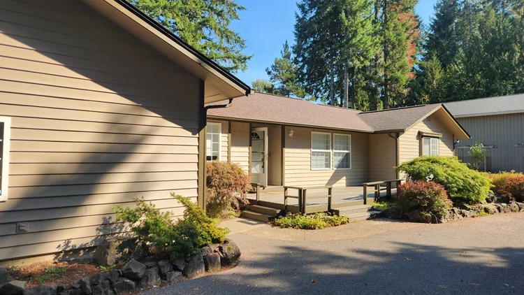 Front exterior of a tan single-story Hoodsport home with a covered porch and shrubs
