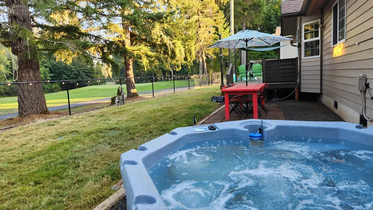 Hot tub on gravel beside a lawn and red picnic table, with the fairway behind the fence