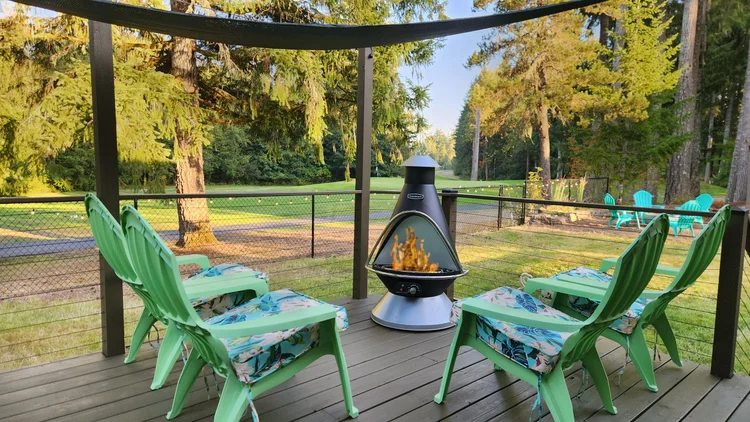 Covered deck with green Adirondack chairs around a chimney fire pit facing the golf course