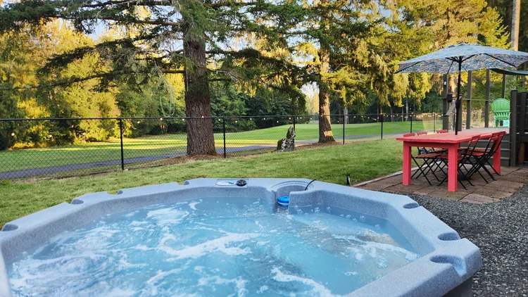 Backyard hot tub beside a red picnic table and umbrella, with golf course fairway beyond the fence
