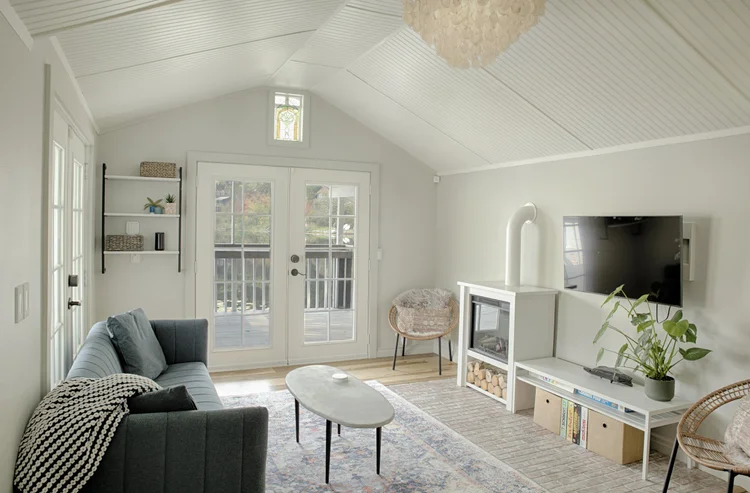 Living room with vaulted white ceiling, gray sofa, electric fireplace and French doors to the deck