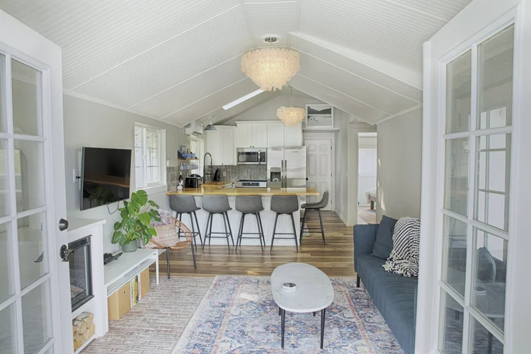 Open living area facing a kitchen with butcher block peninsula, four bar stools and shell chandeliers