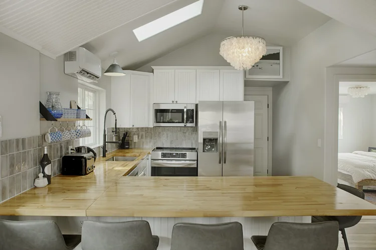 Kitchen with butcher block peninsula, white cabinets, skylight and stainless refrigerator