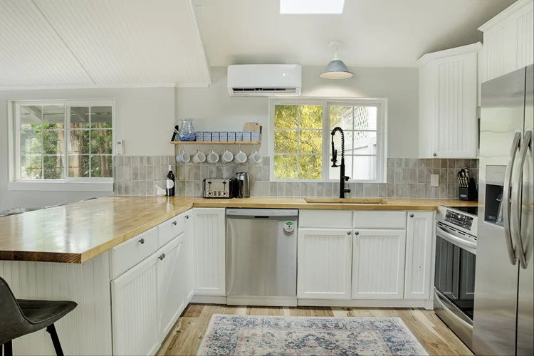 White kitchen with butcher block counters, black faucet, tile backsplash and mini split heat pump