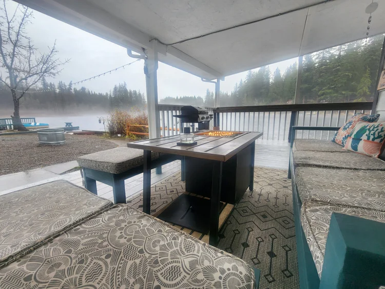 Covered patio seating around a lit fire table on a misty, rainy lake morning