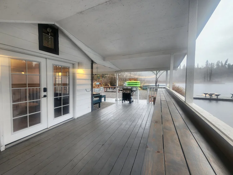 Long covered deck with French doors, gray plank floor and misty lake view