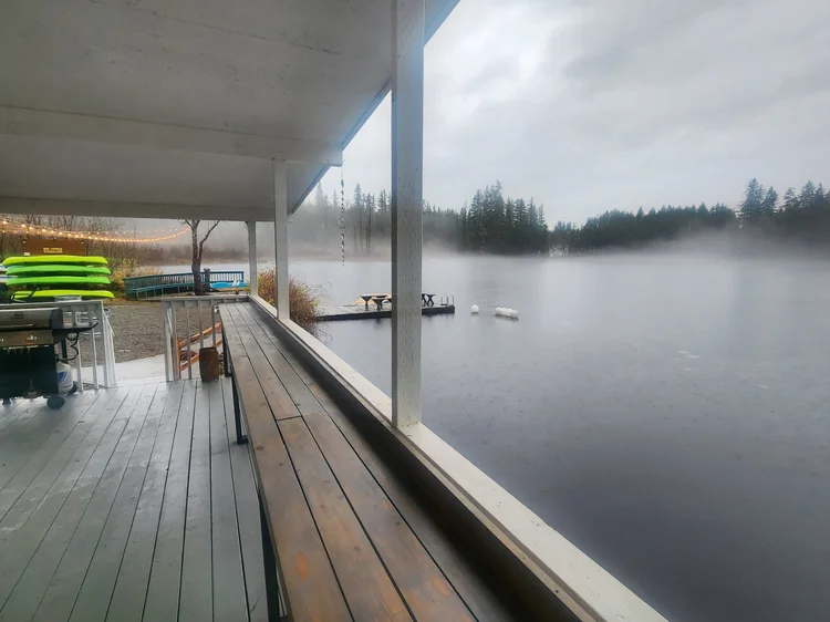 Covered deck with wood bar ledge along the railing overlooking a foggy lake in the rain