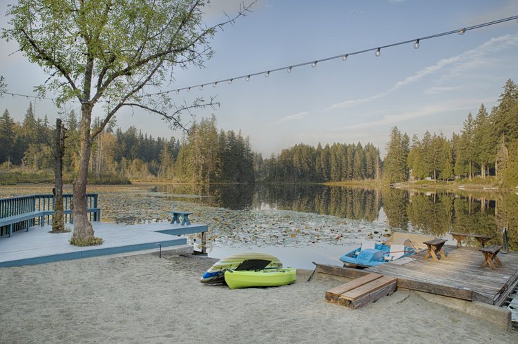Sandy lakeside beach with kayaks, a paddle boat dock and string lights over calm water