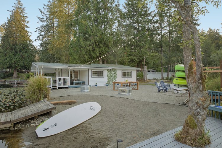 Lakeside Wonderland cottage behind a sandy beach with paddleboard, tall evergreens and string lights