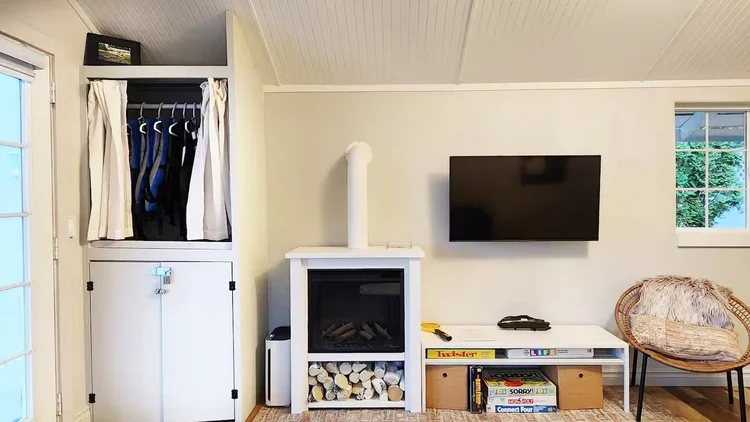 Living room wall with closet, electric fireplace with log storage, mounted TV and board games