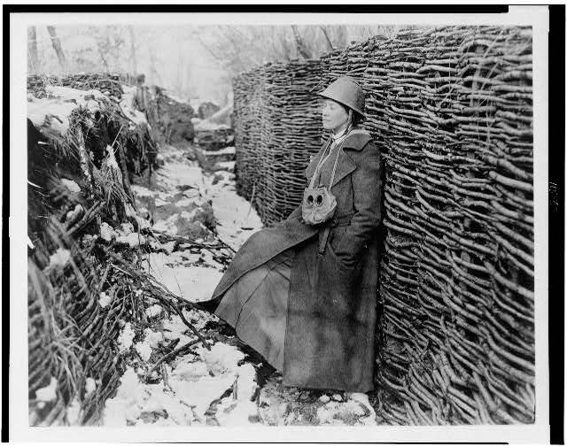 Helen Johns Kirtland in trench during World War I; she is wearing a helmet and great coat, and has a gas mask hanging around her neck . Between 1914 and 1918.