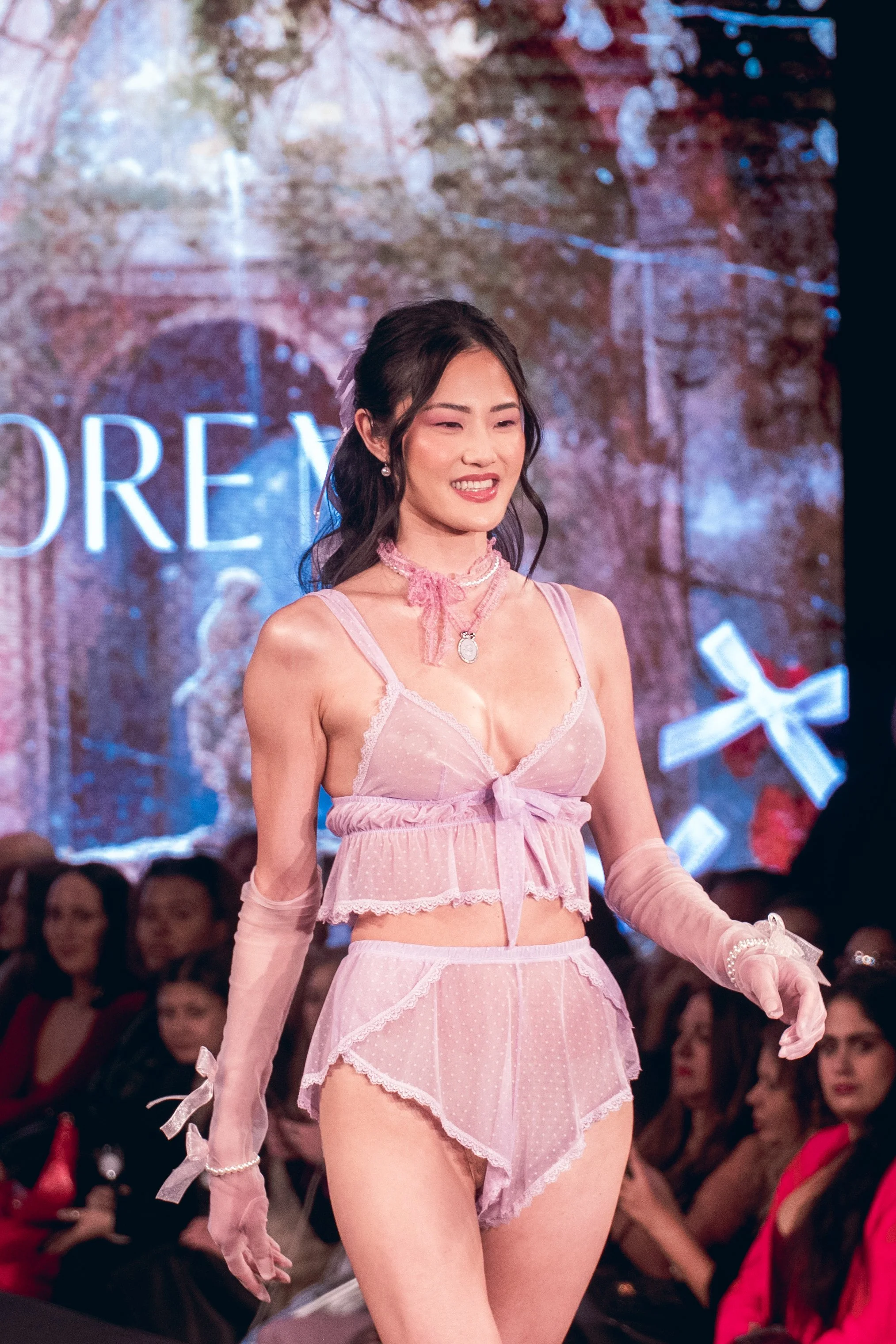 Smiling model in a pink sheer outfit poses on the Adore Me runway at New York Fashion Week 2024