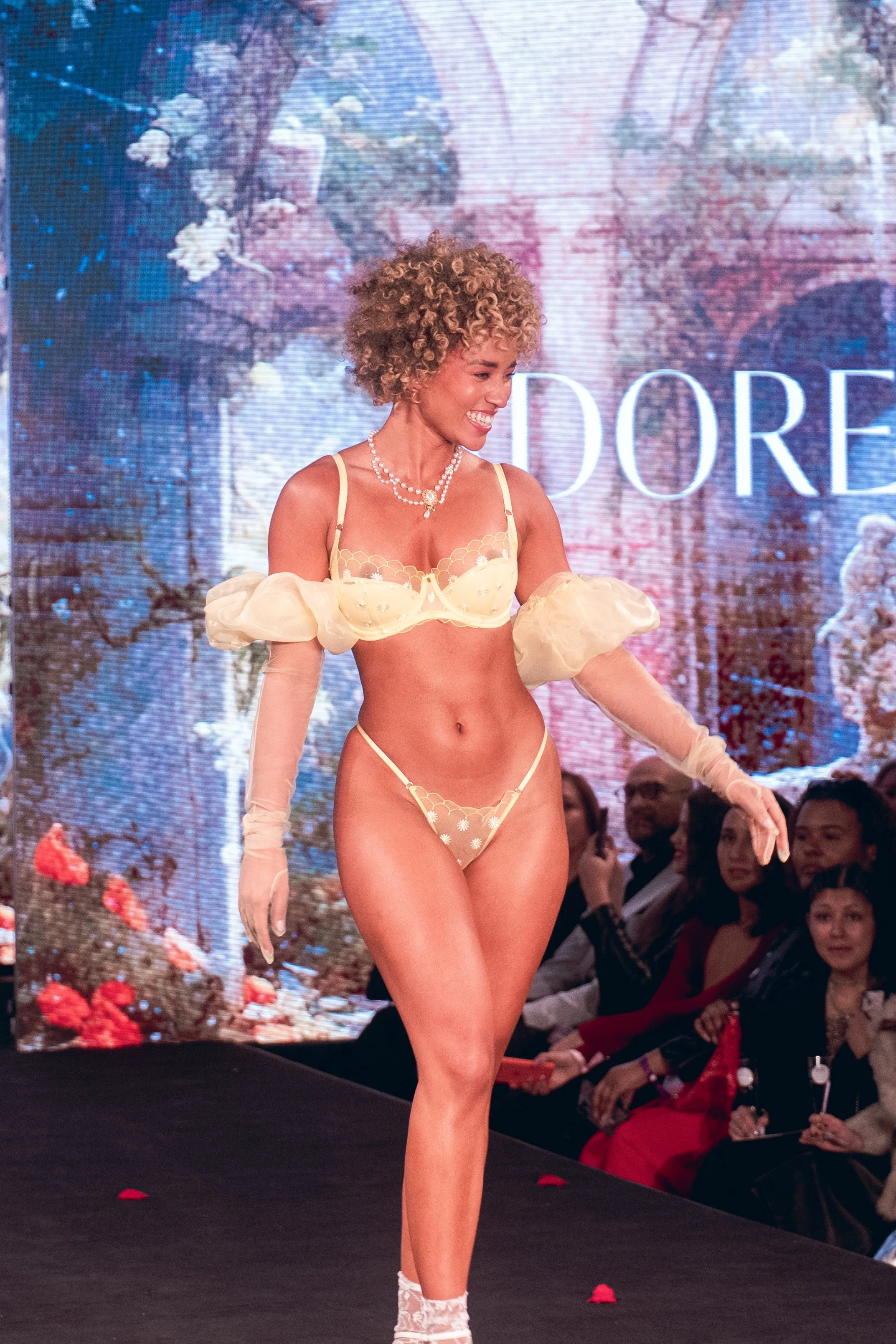 Curly-haired model in a peach two-piece outfit poses on the Adore Me runway at New York Fashion Week 2024