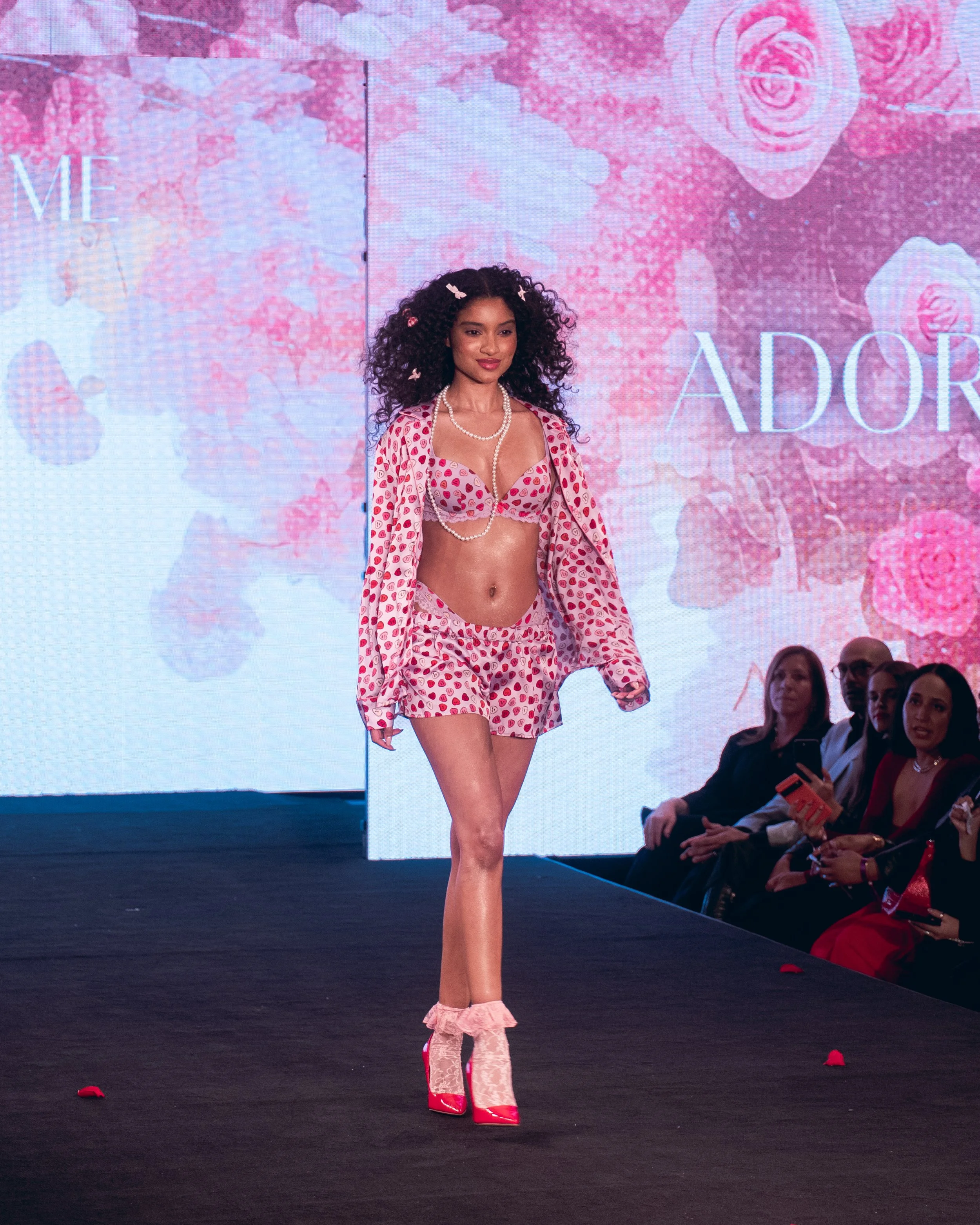 Curly-haired model in a pink patterned outfit walks the Adore Me runway at New York Fashion Week 2024