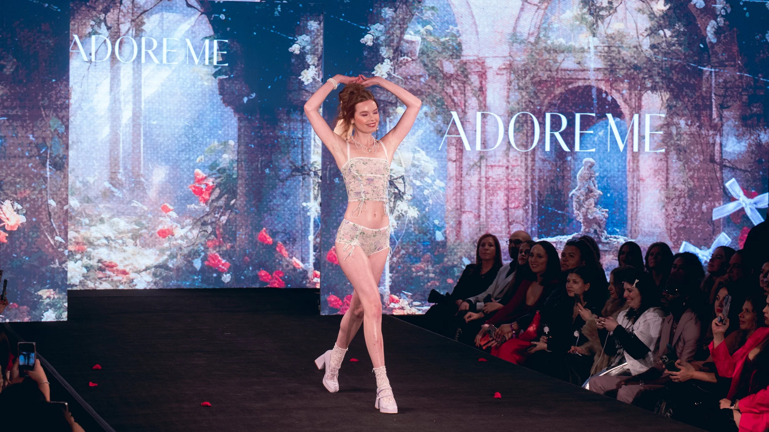 Model in white lingerie raises both arms on the Adore Me runway at New York Fashion Week 2024